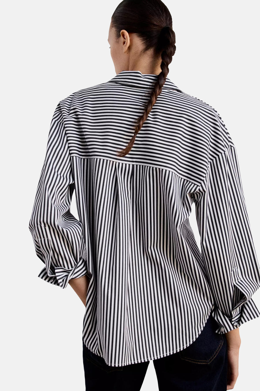 Black and white striped long-sleeve blouse with pleated back, shown from rear on model wearing dark jeans