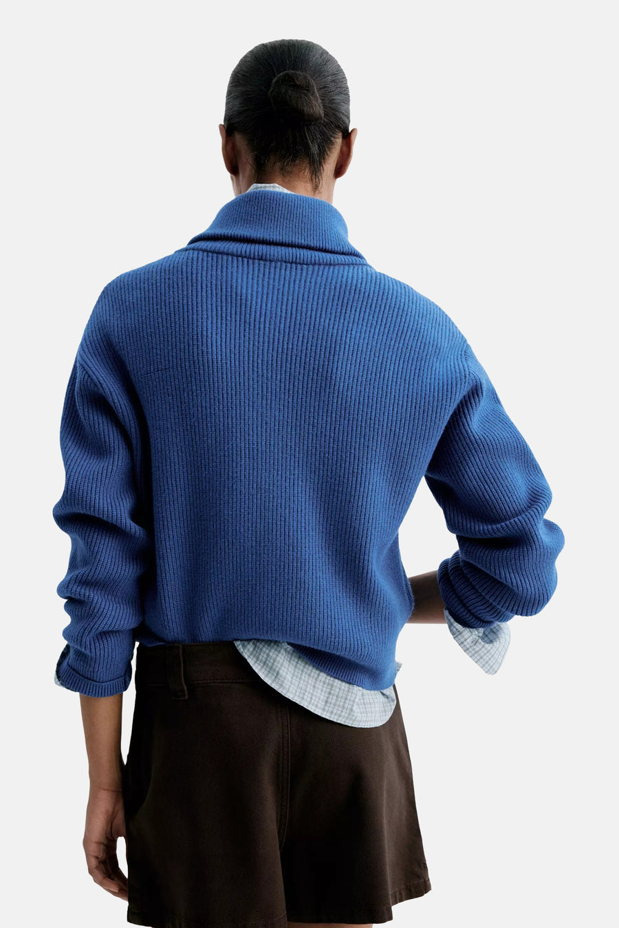 Blue ribbed turtleneck sweater back view, worn with rolled sleeves over a checkered shirt and dark shorts