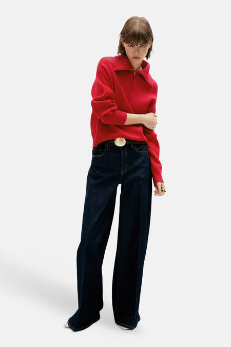 Pull col montant rouge en maille rib par MANGO, porté avec un jean large et une ceinture à boucle dorée, vue de face.