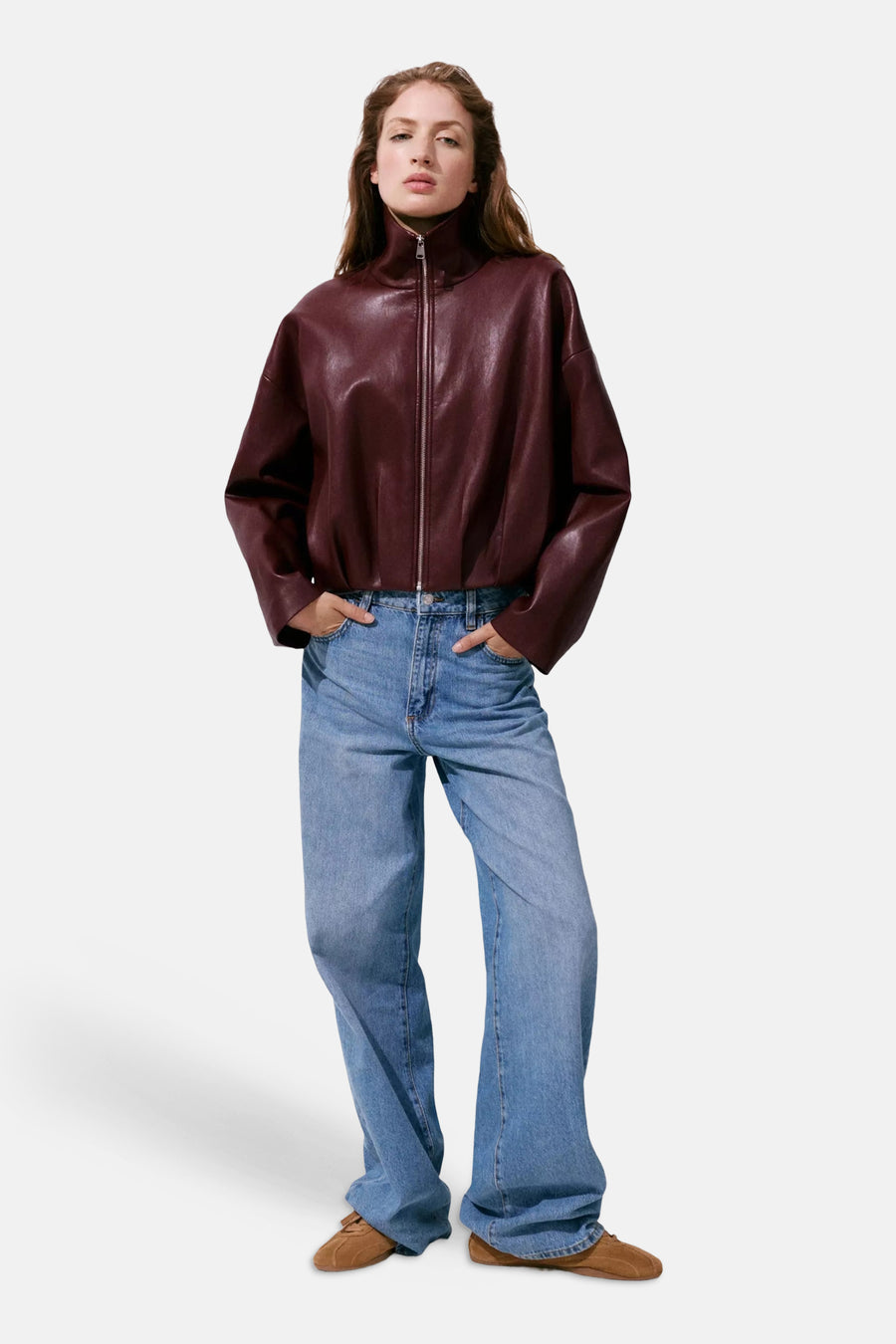 Bordeaux leather bomber jacket with high collar and front zipper, worn with blue jeans and brown shoes, full-length lifestyle view