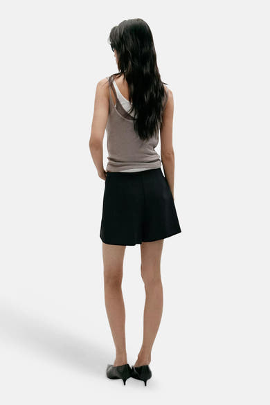 Black A-line skirt from back view, worn with taupe tank top and black heels, smooth fabric, mid-thigh length