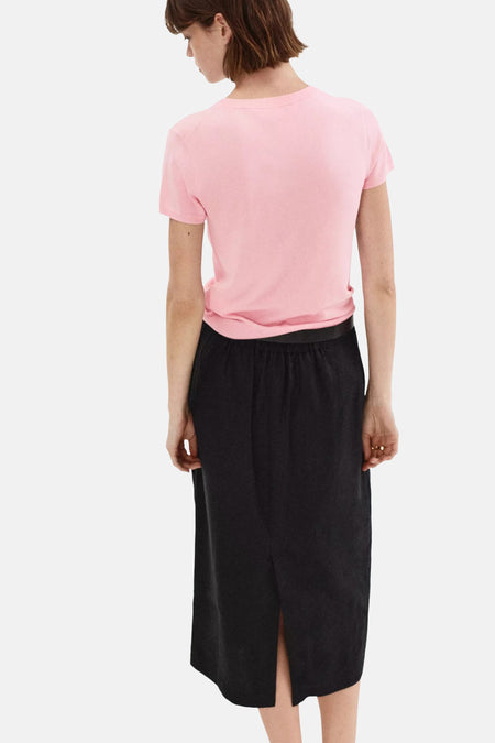 Pink short-sleeve knit top with round neckline, back view, worn with black skirt and belt, soft texture, casual fit