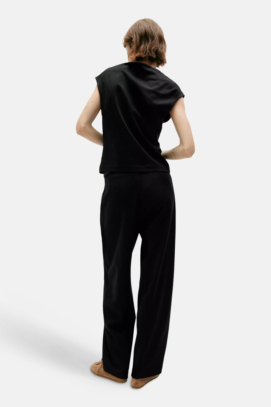 Black sleeveless top with relaxed fit and rounded neckline, back view, paired with black trousers and tan moccasins