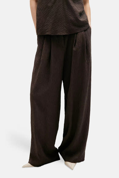 Brown textured wide-leg chinos with vertical ribbed pattern, shown front view on model wearing matching top and white pointed-toe shoes.