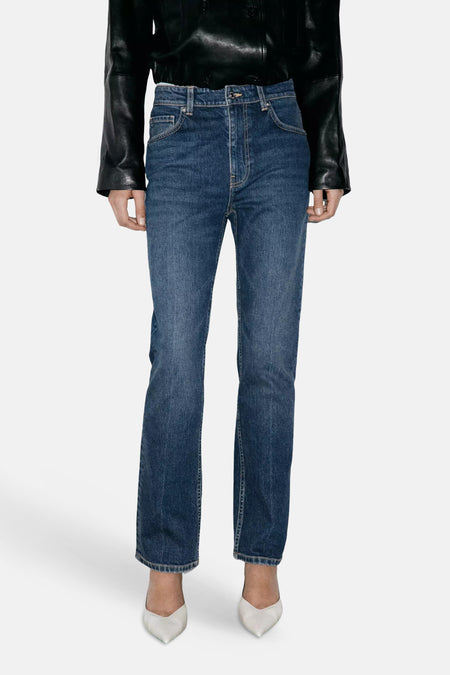 Jeans slim en denim bleu foncé par MANGO, coupe droite, poches avant, portés avec veste en cuir noir et escarpins blancs, vue de face.