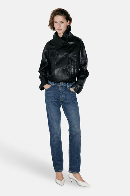 Jeans slim en denim bleu foncé par MANGO, coupe droite, portés avec une veste en cuir noir et escarpins blancs, vue de face.
