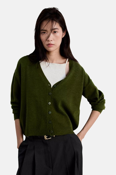 Cardigan vert en maille fine à col en V par MANGO, boutonné, porté avec un haut blanc et un pantalon noir, vue de face