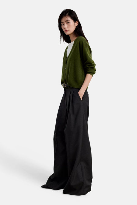 Cardigan vert en maille douce de MANGO, vue de profil, porté avec pantalon noir ample et ceinture fine