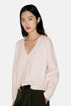 Cardigan rose en maille fine à col en V par MANGO, porté avec un pantalon noir et une ceinture en cuir, vue de face.