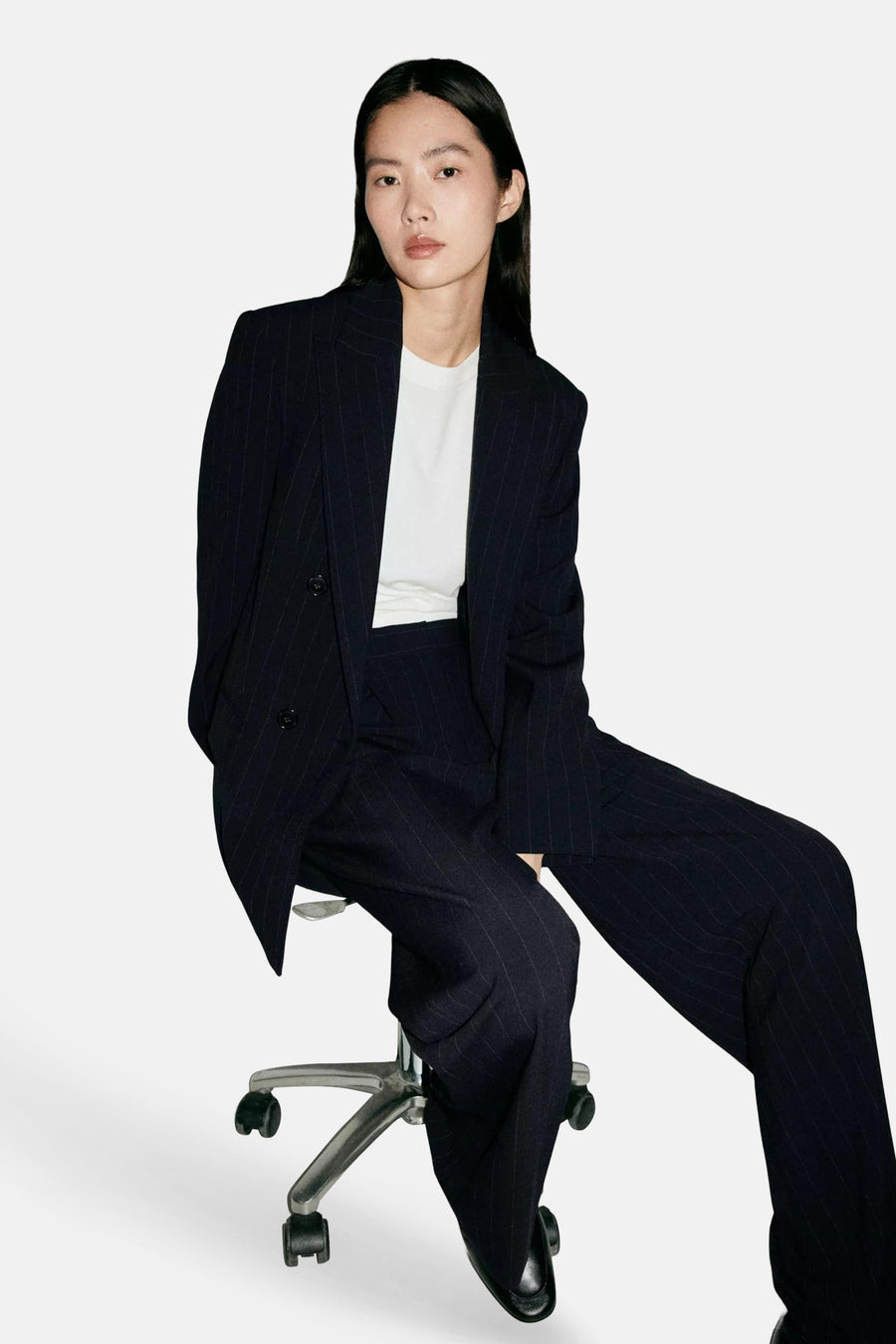Pantalon de costume bleu marine à fines rayures, par MANGO, porté avec veste assortie, vue lifestyle sur chaise pivotante