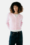 Gilet rose en tricot côtelé par MANGO, boutonné, porté avec un t-shirt blanc et un jean foncé, vue de face