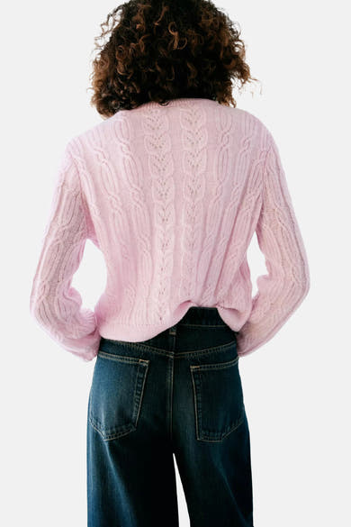 Gilet rose en tricot côtelé par MANGO, vue arrière avec motif torsadé et détails ajourés, porté avec un jean bleu foncé