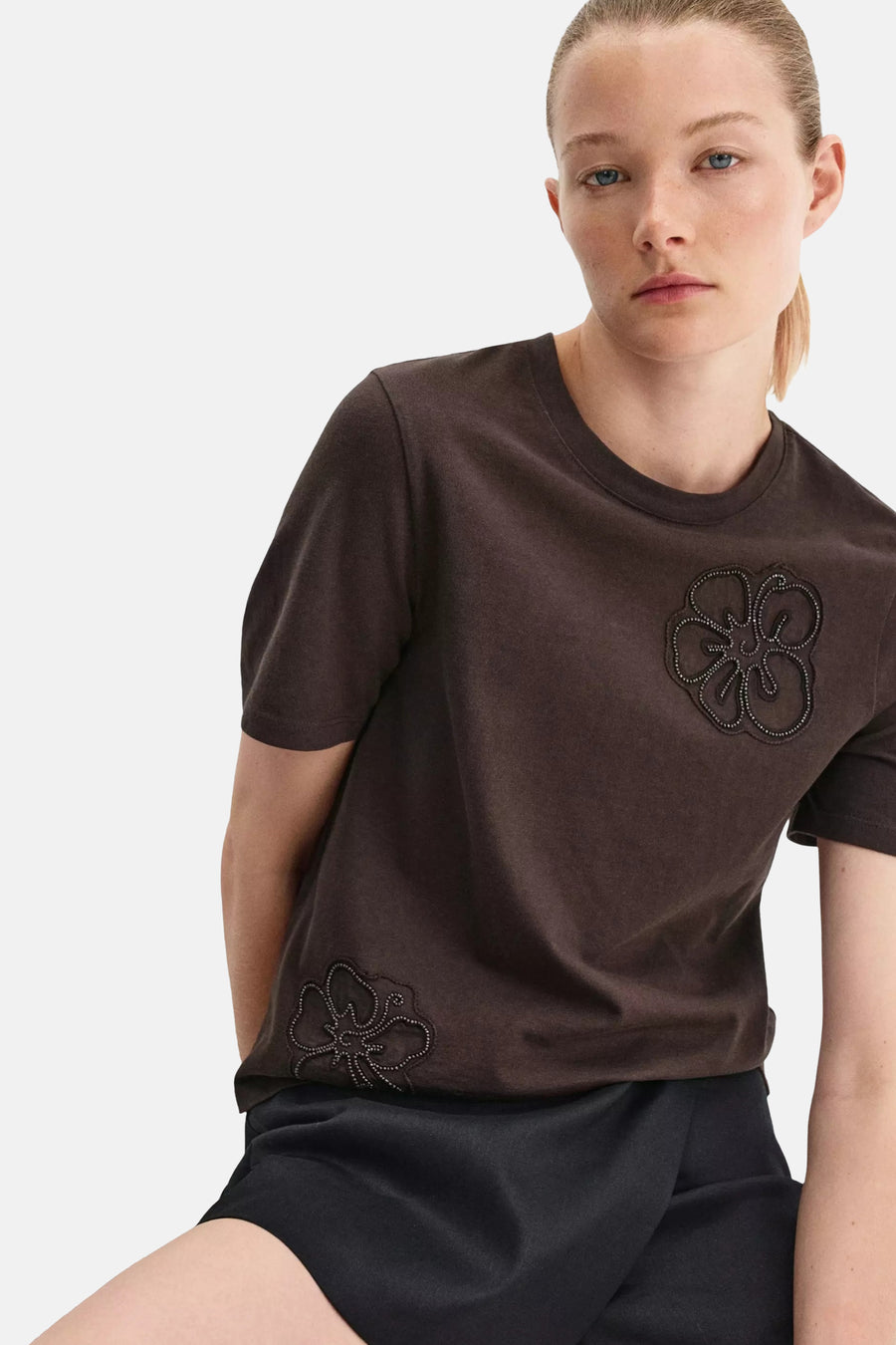 Brown short-sleeve T-shirt with floral beadwork, worn by model in lifestyle pose, paired with dark skirt.