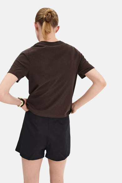 Brown short-sleeve t-shirt back view, soft cotton fabric, model wearing black shorts and gold cuff bracelet