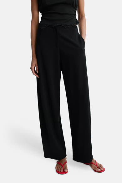 Black wide-leg elastic waist trousers with lace trim at waist, worn with black top and red flip-flops, front view