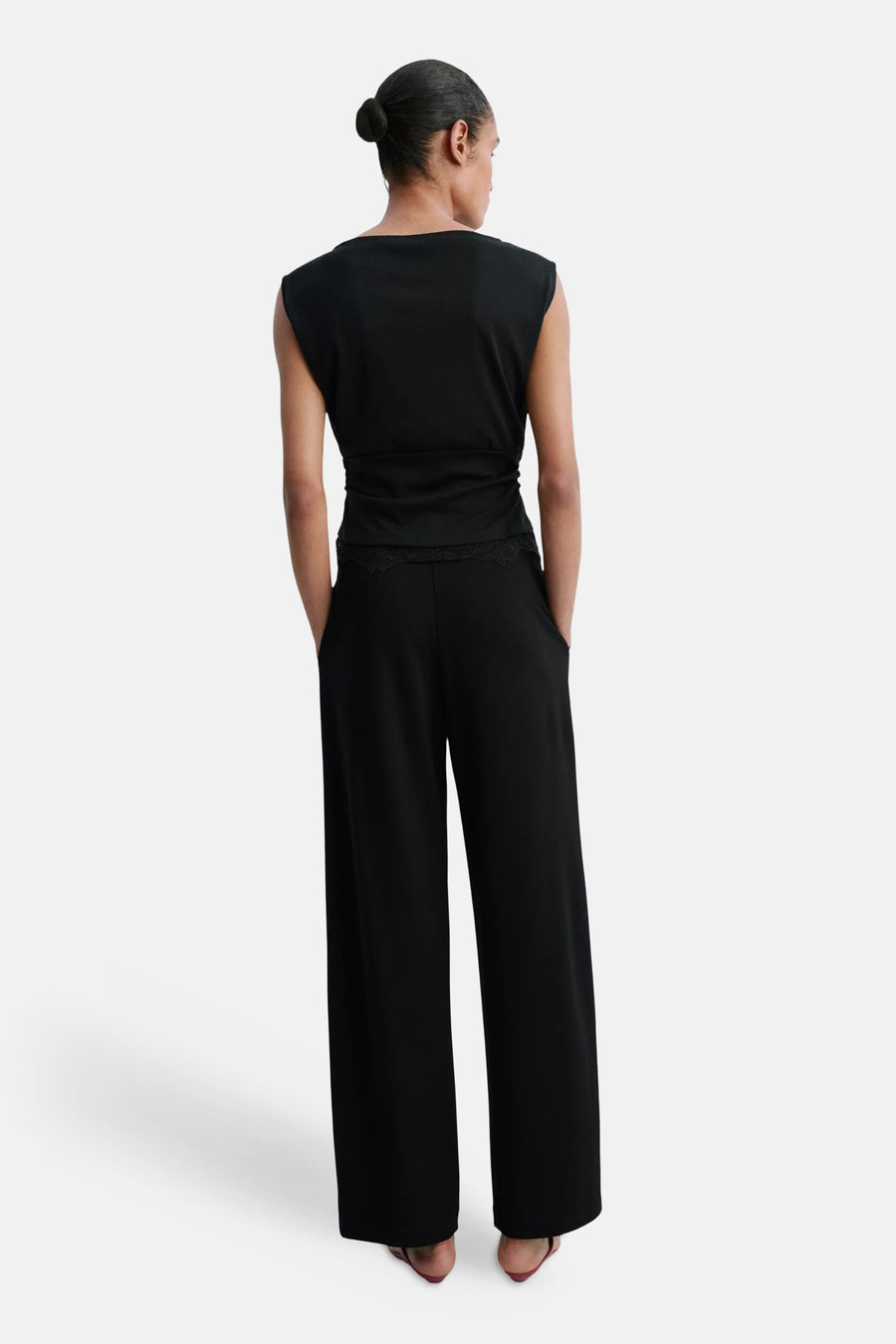 Black wide-leg elastic waist trousers with lace trim at waist, back view, worn with sleeveless top and red heels