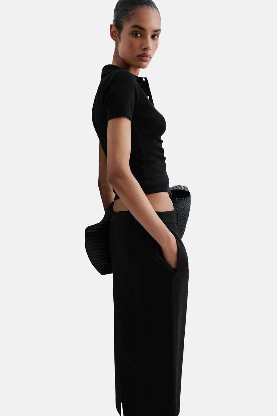Black ribbed knit cardigan with button front, side view on model wearing black cropped top and wide-leg pants, holding woven bag.