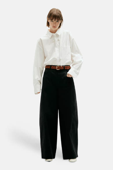 Pantalon cargo noir ample par MANGO, porté avec chemise blanche et ceinture marron tressée, vue de face.