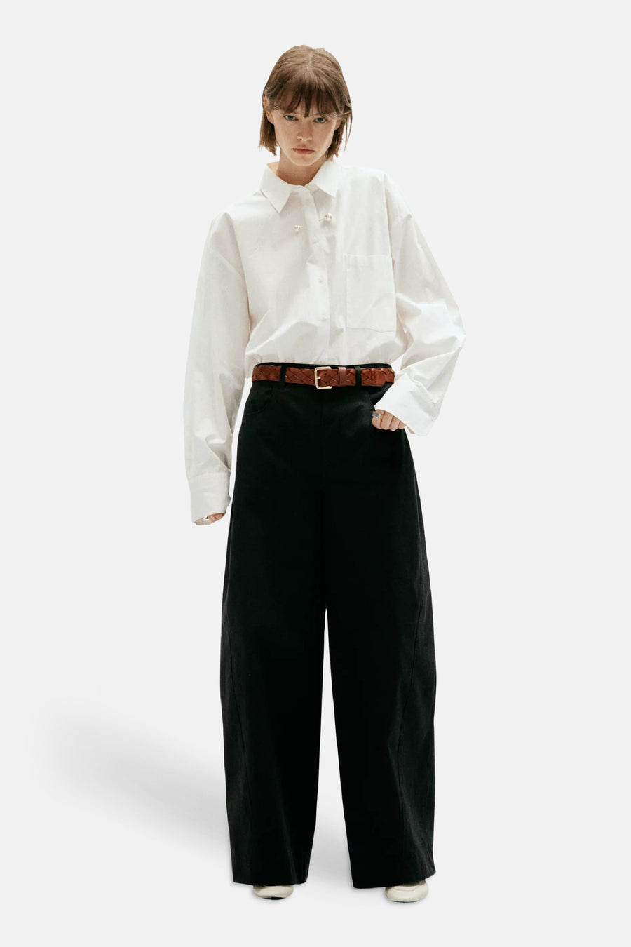 Pantalon cargo noir ample par MANGO, porté avec chemise blanche et ceinture marron tressée, vue de face.