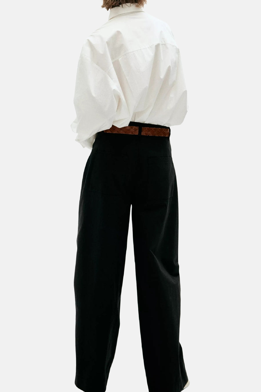 Pantalon cargo noir ample, vue arrière, par MANGO, avec ceinture marron tressée et chemise blanche fluide