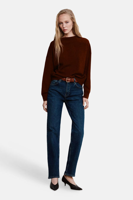 Pull col rond marron par MANGO, en maille douce, porté avec jeans bleu foncé et ceinture tressée, vue de face.