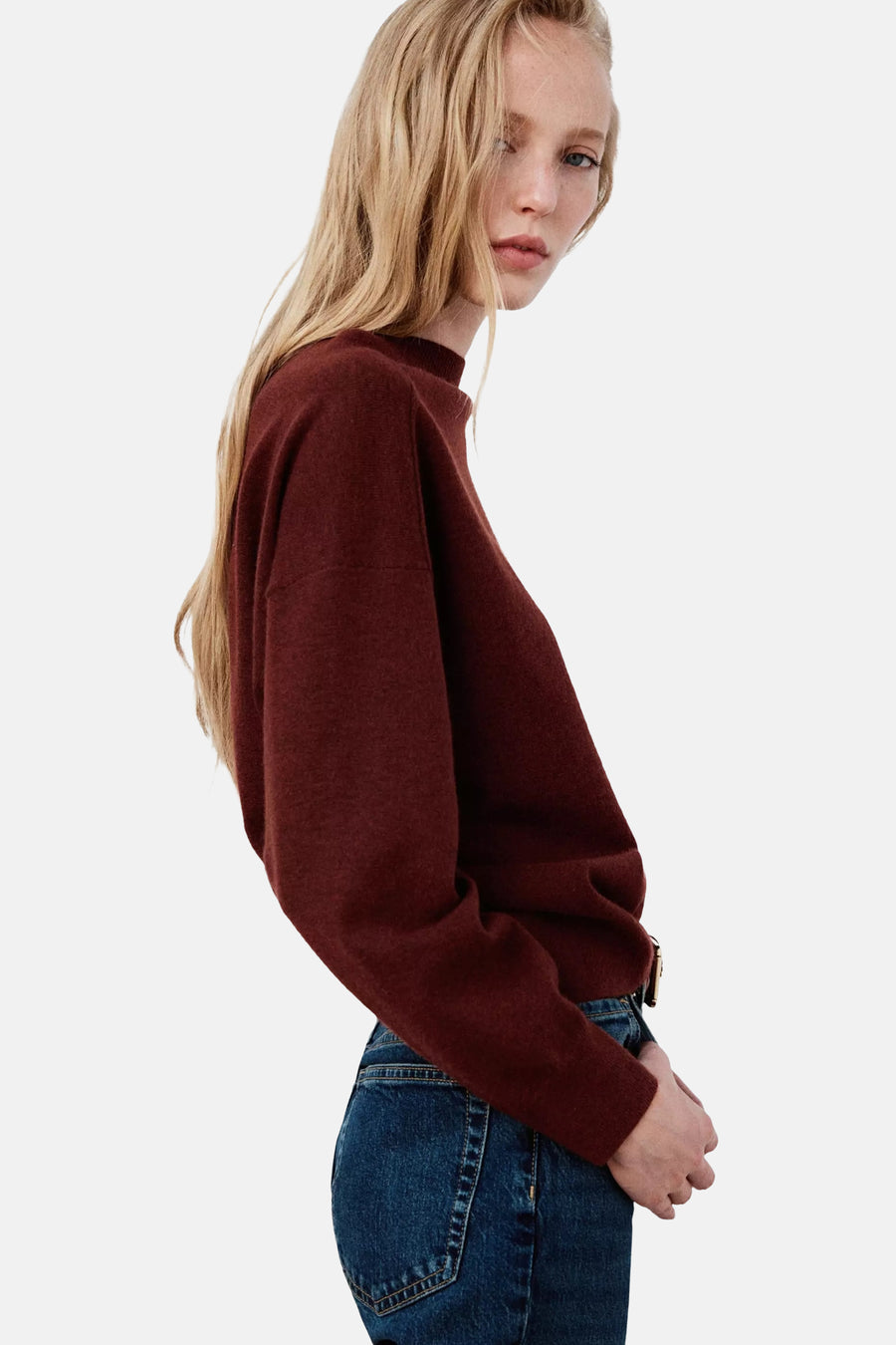 Pull col rond marron foncé de MANGO, vue de profil, matière douce et ajustement ample, porté avec un jean bleu.