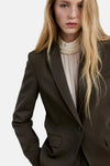 Khaki blazer with structured shoulders and single-button front, worn over cream turtleneck, side view close-up