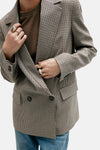 Multicolored houndstooth blazer with double-breasted front, structured shoulders, and flap pockets, worn over olive top with blue jeans, cropped front view