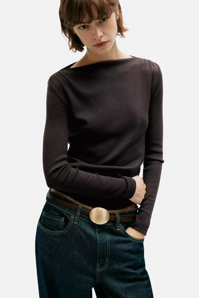 Brown long-sleeve ribbed top with off-shoulder neckline, worn with dark jeans and brown belt featuring round buckle, front view