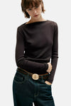Brown long-sleeve ribbed top with off-shoulder neckline, worn with dark jeans and brown belt featuring round buckle, front view