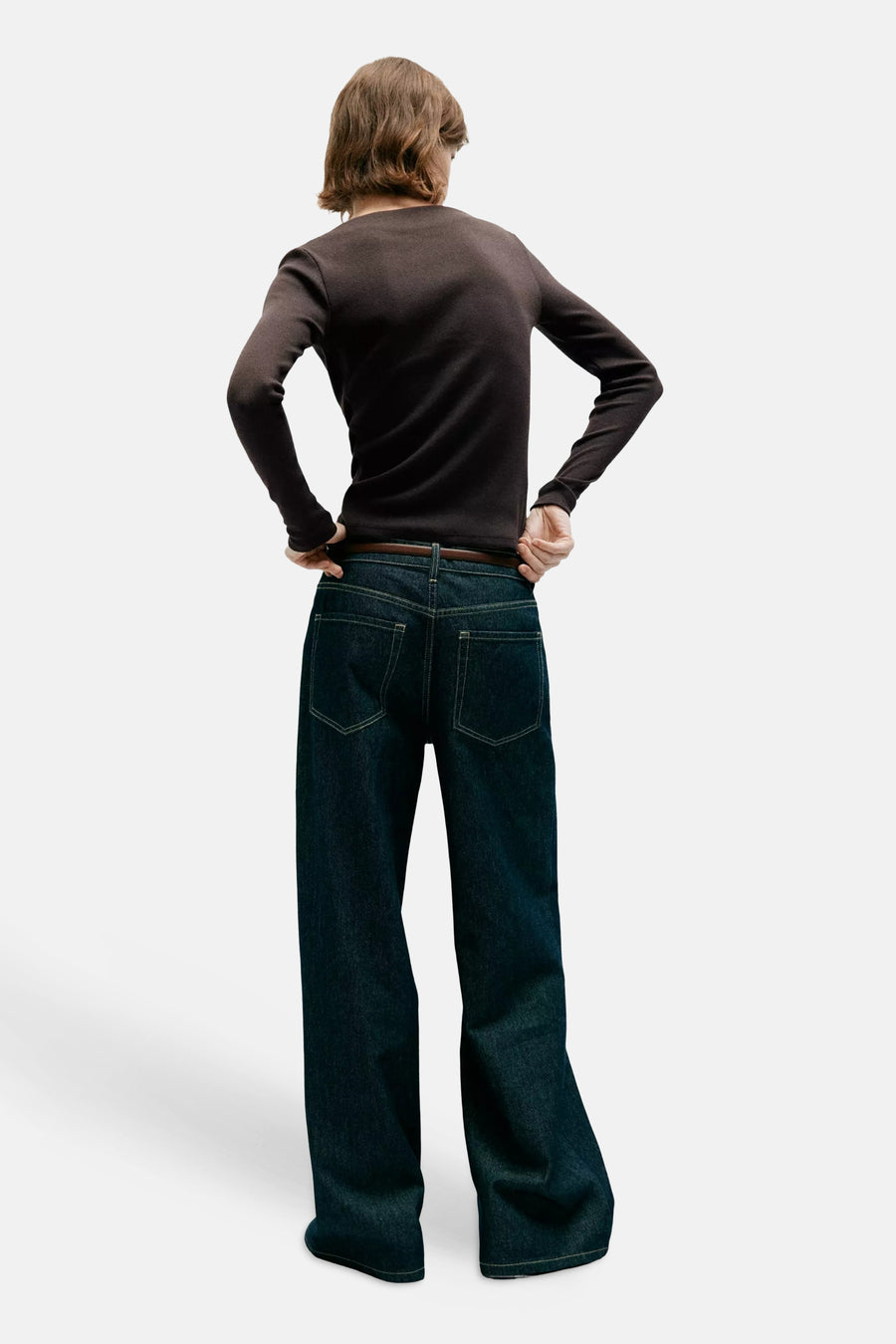Brown long-sleeve t-shirt from back view, fitted with slim sleeves, worn with dark denim jeans and brown belt.