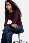Bordeaux long-sleeve ribbed T-shirt with boat neckline, worn with dark blue jeans, side view on stool