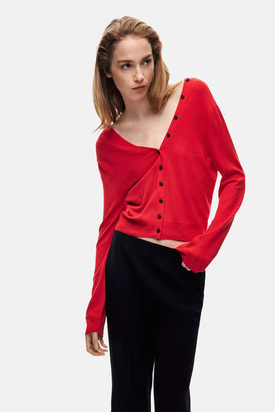 Cardigan rouge à boutons noirs de MANGO, coupe asymétrique, porté avec pantalon noir, vue de profil