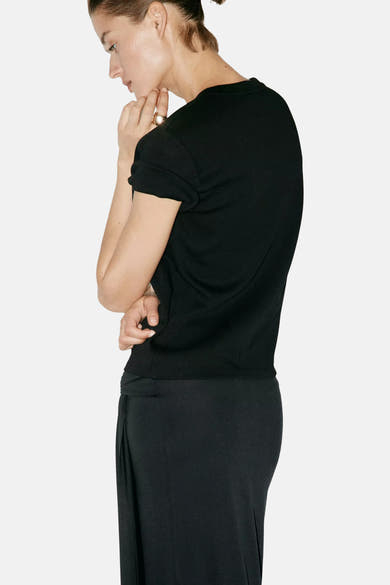 Black short-sleeve t-shirt with ribbed hem and rolled sleeves, side view on model wearing black pants