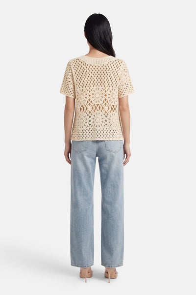Beige trui met korte mouwen van Terra di Siena, met een opengewerkt bloemenhaakpatroon en gedragen over een high-waisted jeans.