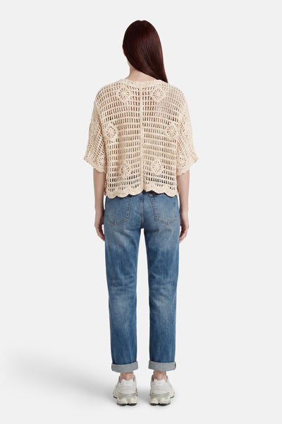 Ecru crocheted gilet with floral pattern and scalloped hem, back view, worn with blue jeans and white sneakers