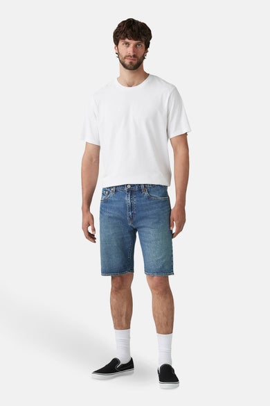 Korte spijkerbroek in middellichte denim van Levi's®, gedragen met een effen wit T-shirt, witte sokken en zwarte schoenen.