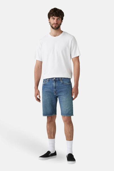 Korte spijkerbroek in middellichte denim van Levi's®, gedragen met een effen wit T-shirt, witte sokken en zwarte schoenen.