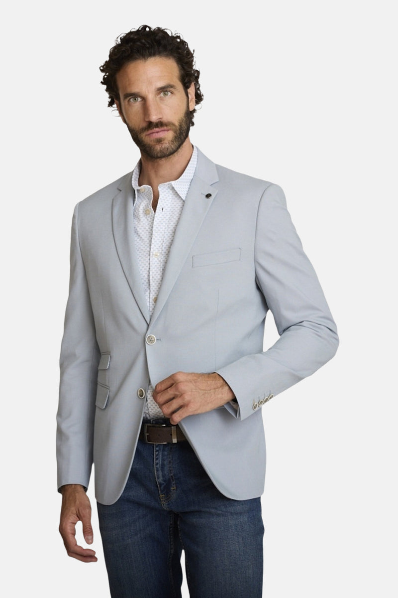 Blauwe blazer van DELAHAYE met bloemenvoering, gedragen over een overhemd met patroon en een spijkerbroek met riem.