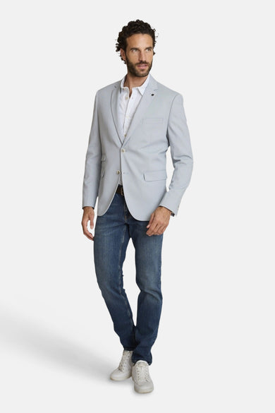 Lichtblauwe blazer van DELAHAYE, gedragen met een overhemd met patroon en een spijkerbroek, witte sportschoenen.