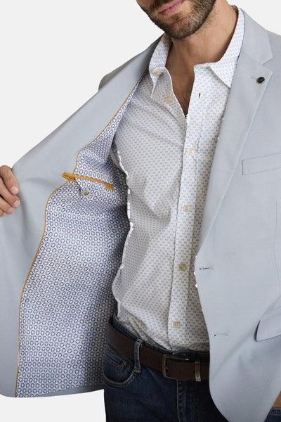 Blazer bleu de DELAHAYE avec doublure à motifs floraux, porté sur une chemise à motifs et un jean avec ceinture.