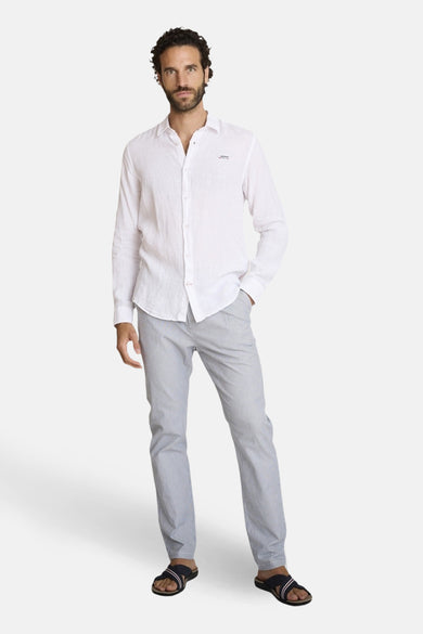 Chemise blanche à manches longues de DELAHAYE, en lin, portée avec un pantalon rayé gris et des sandales noires.