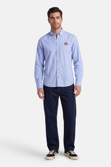 Blauw DELAHAYE overhemd met lange mouwen, met een geknoopte kraag en embleem, gedragen met een spijkerbroek en sneakers.