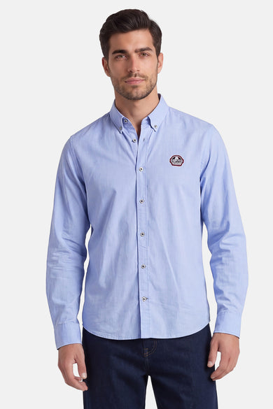 Blauw overhemd met lange mouwen van DELAHAYE met een knoopkraag en een embleem op de borst, gedragen met een donkere spijkerbroek.
