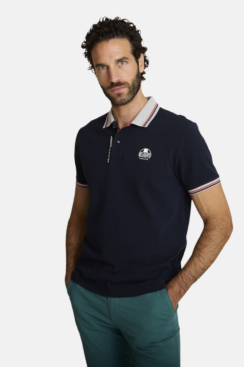 Polo bleu marine par DELAHAYE, avec col rayé et logo sur la poitrine, porté avec un pantalon vert.