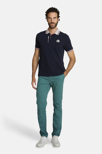 Polo bleu marine de DELAHAYE avec col et manches à rayures contrastées, porté avec un pantalon vert et des baskets blanches.
