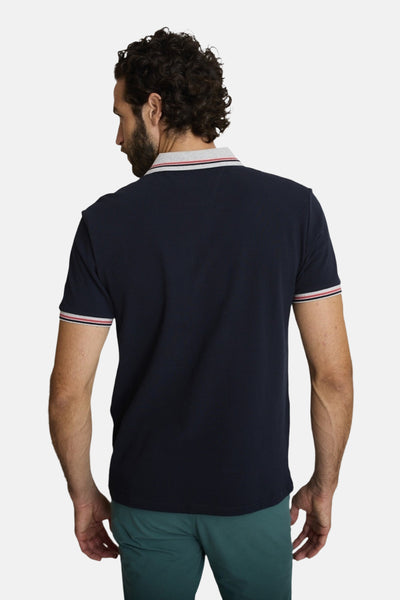 Polo bleu marine de DELAHAYE, avec col et manches à rayures rouge et blanc, porté avec un pantalon vert.