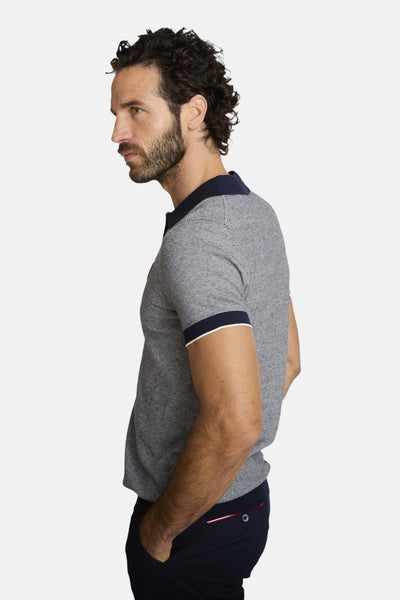 Pull bleu col O de DELAHAYE, en maille piquée, avec manches courtes à bordures contrastées et pantalon marine en arrière-plan.