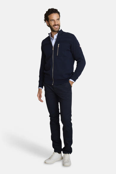 Blauwe bodywarmer van DELAHAYE, met zilveren ritssluiting en borstzakdetail met rits, gedragen met een lichtblauw overhemd en een marineblauwe chino.