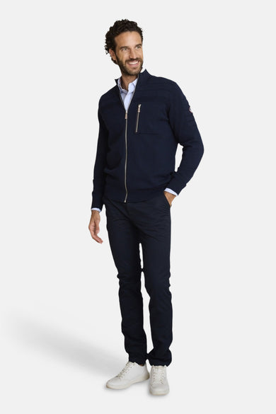Blauwe bodywarmer van DELAHAYE, met zilveren ritssluiting en borstzakdetail met rits, gedragen met een lichtblauw overhemd en een marineblauwe chino.